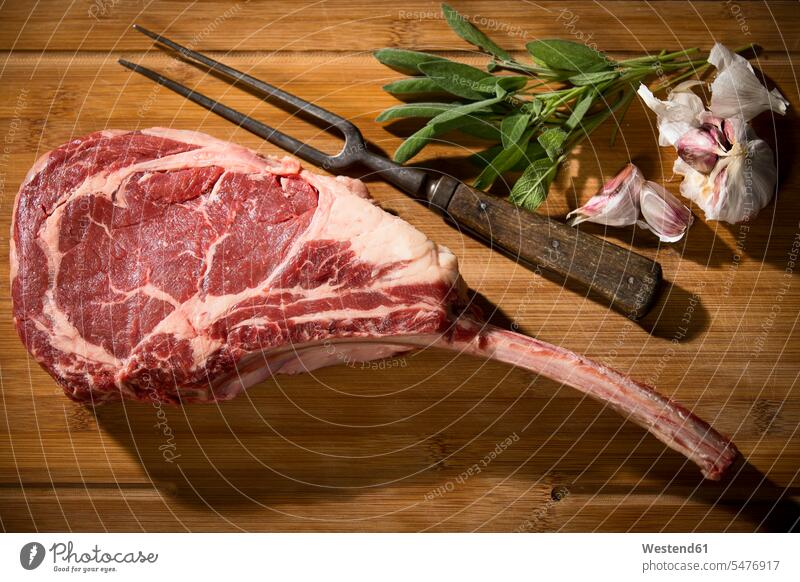 Raw tomahawk steak, garlic and herbs meat fork Garlic Bulb Garlic Bulbs Garlic Tuber ingredient ingredients culinary herb culinary herbs kitchen herb