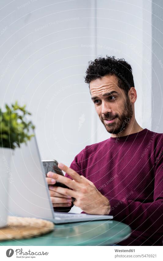 Young man stting at table at home using laptop and cell phone human human being human beings humans person persons celibate celibates singles solitary people