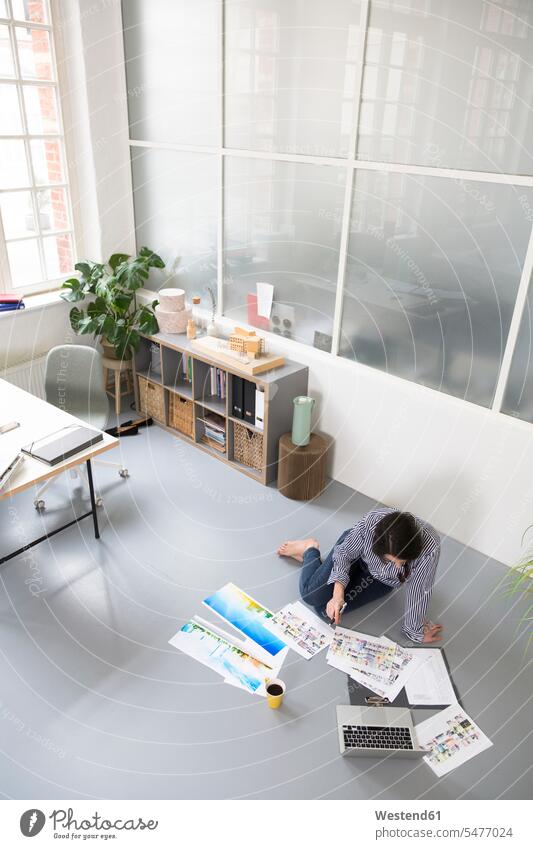 Casual woman with sheets of paper and laptop sitting on the floor in a loft office females women lofts casual floors Laptop Computers laptops notebook Seated