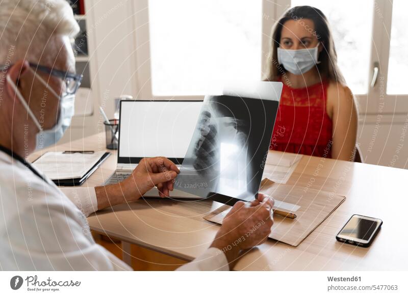 Doctor looks at medical x-ray of human neck while sitting in clinic color image colour image indoors indoor shot indoor shots interior interior view Interiors