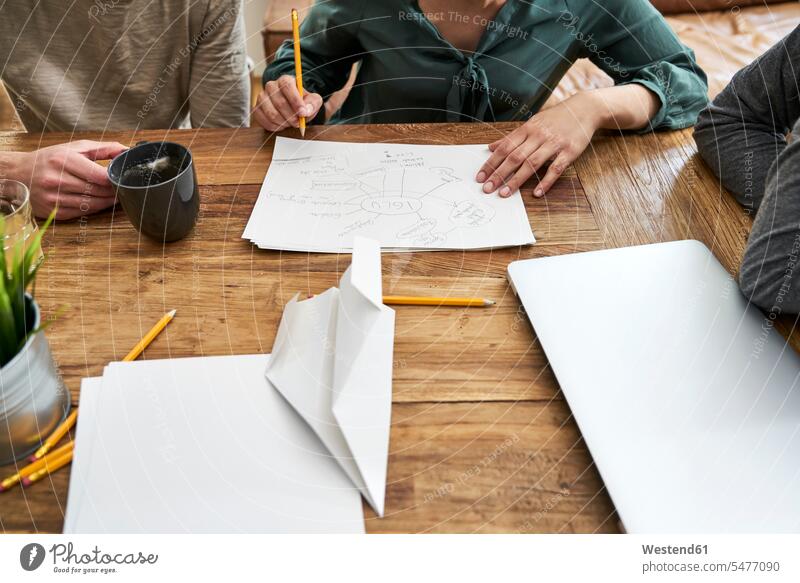 Coworkers working together and taking notes at table in office At Work offices office room office rooms colleagues making a note note taking wooden table