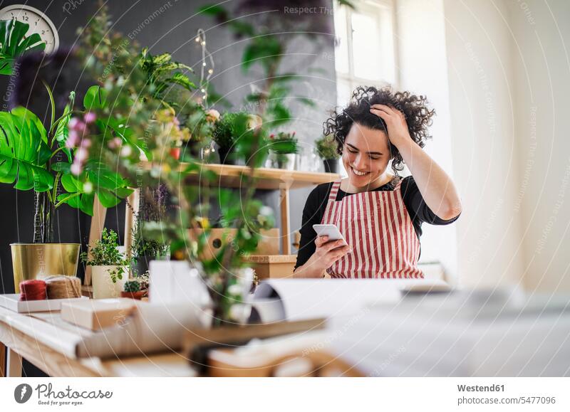 Happy young woman using cell phone in a small shop with plants Occupation Work job jobs profession professional occupation human human being human beings humans