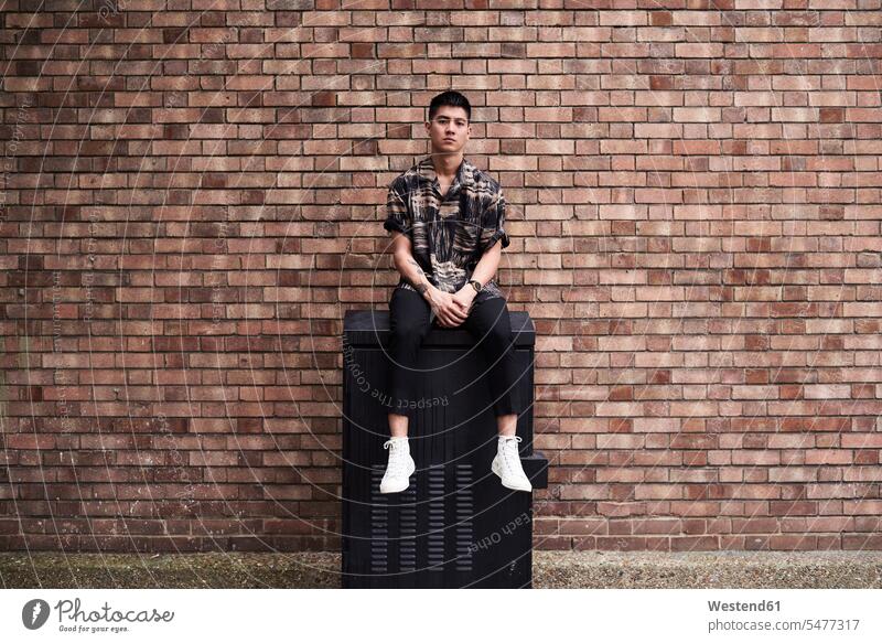 Portrait of young man in front of brick wall shirts Seated sit Distinct individual stylish Body Adornment Skin Art tattoos location shot location shots outdoor