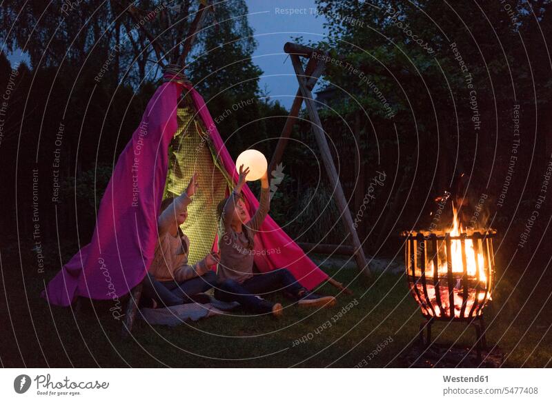 Two girls standing in front of tipi, holding lamp as moon light lights Camp Fire Campfire Bonfire playing Holding Aloft garden gardens domestic garden tent