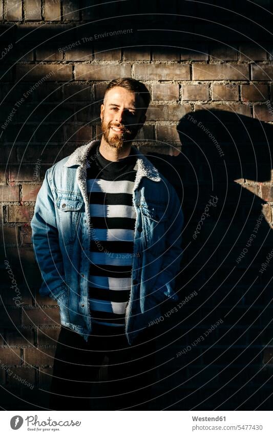 Portrait of a smiling man standing at a brick wall in shadow brick walls men males portrait portraits smile Adults grown-ups grownups adult people persons