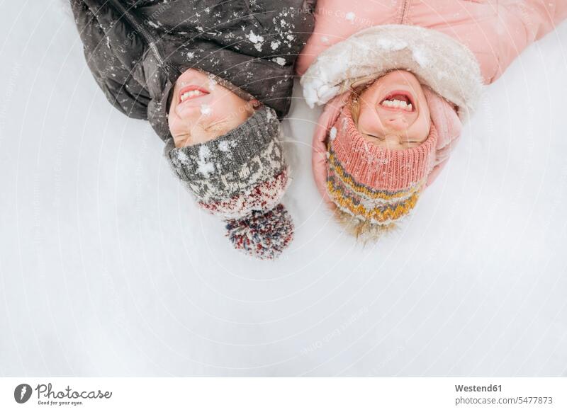 Portrait of two siblings lying on snow smile seasons hibernal delight enjoyment Pleasant pleasure Cheerfulness exhilaration gaiety gay glad Joyous merry happy