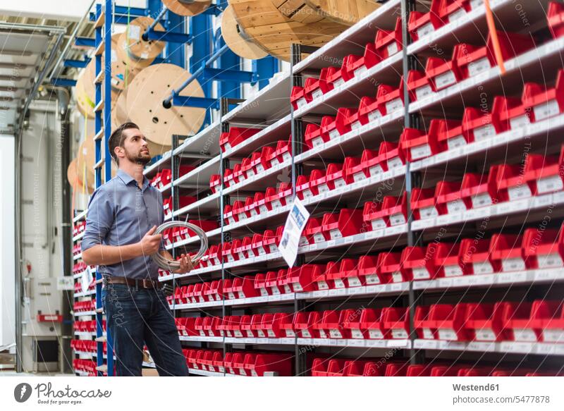 Man standing at shelf in storehouse holding cable man men males Shelve rack racks shelves power cord cables storage room stockroom storeroom Adults grown-ups