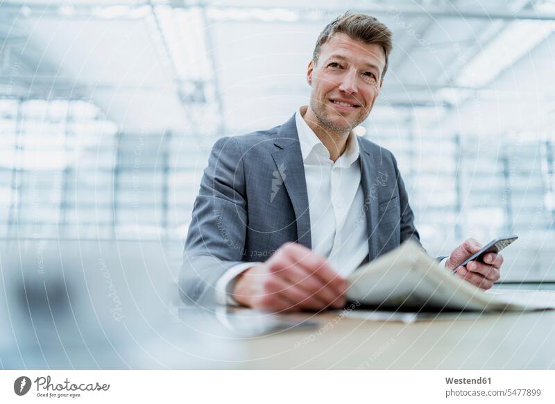 Smiling businessman with cell phone and newspaper in a cafe Germany wireless Wireless Connection Wireless Technology Wireless Communication confidence confident