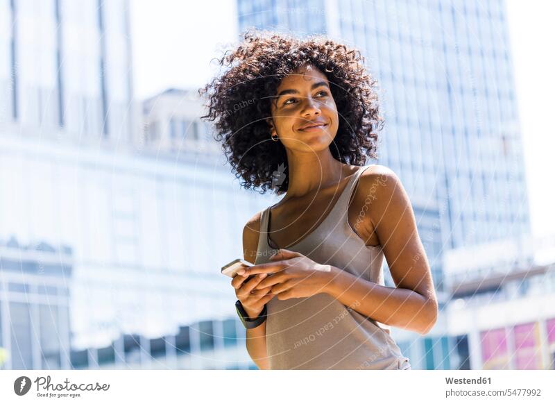 Germany, Frankfurt, portrait of smiling young woman with curly hair in front of skyscrapers multistory building high rise portraits curls smile females women