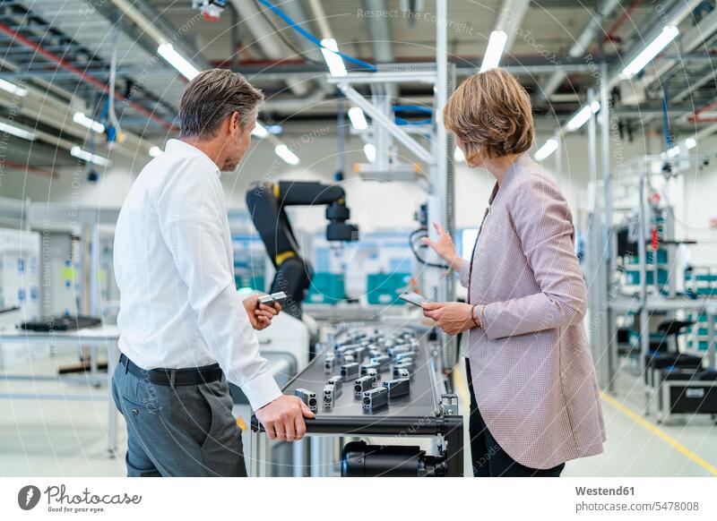 Businessman and businesswoman talking in a modern factory hall business life business world business person businesspeople associate associates