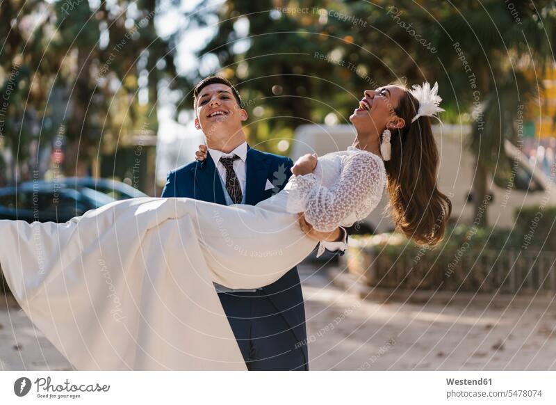 Young groom picking up cheerful bride in park color image colour image outdoors location shots outdoor shot outdoor shots day daylight shot daylight shots
