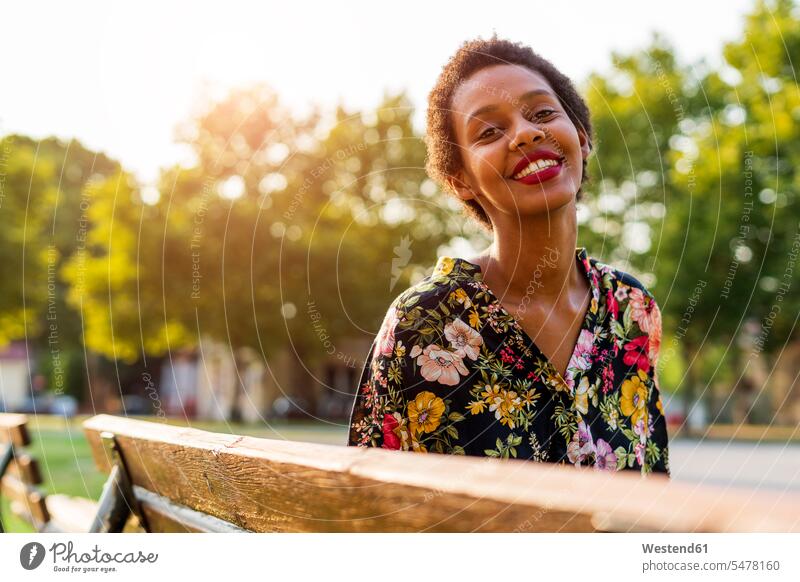 Portrait of smiling young woman on bench in a park laughing Laughter parks females women portrait portraits smile benches positive Emotion Feeling Feelings