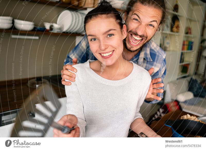 Young couple preparing food together, laughing and pointing with spatula kitchen cooking twosomes partnership couples people persons human being humans