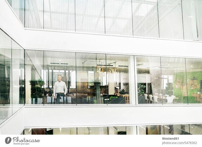 Mature businessman looking out of office building, holding laptop human human being human beings humans person persons caucasian appearance caucasian ethnicity