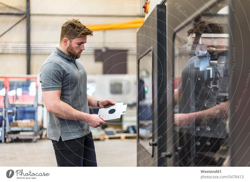 Man examining workpiece on factory shop floor checking examine factories production hall man men males examination examinations Adults grown-ups grownups adult