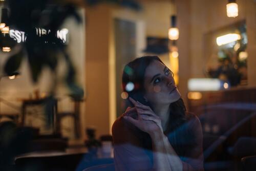 Serious young woman sitting at table in a restaurant looking away Frustration Frustrated frustrating pensive thoughtful Reflective contemplative serious earnest