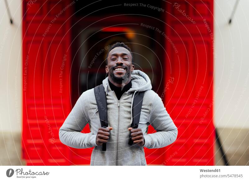 Young man with backpack smiling while standing outdoors color image colour image location shots outdoor shot outdoor shots day daylight shot daylight shots