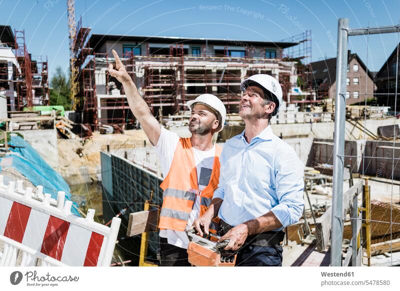 Smiling construction worker talking to man on construction site smiling smile men males Building Site sites Building Sites construction sites builders speaking