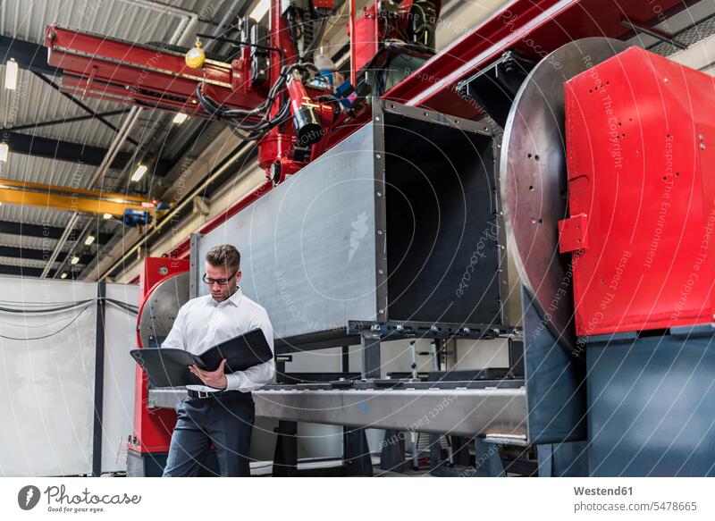 Businessman with folder standing on factory shop floor production hall factories file folders portfolio portfolios files Business man Businessmen Business men