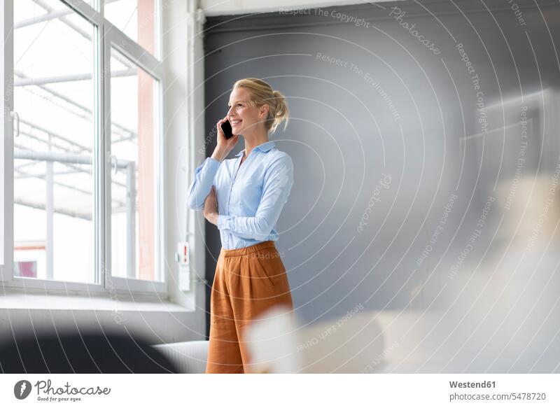 Smiling young businesswoman talking on cell phone in office business life business world business person businesspeople business woman business women