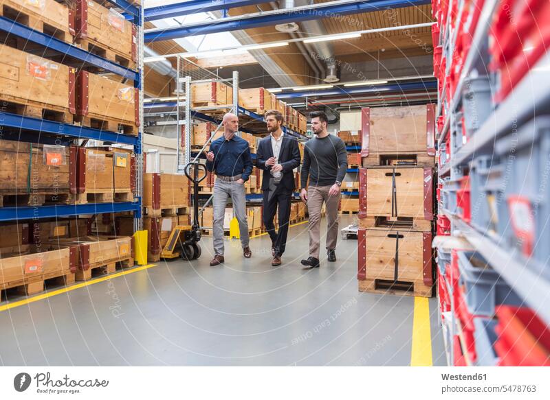 Three men walking and talking in factory storeroom man males storage room stockroom speaking going factories Adults grown-ups grownups adult people persons