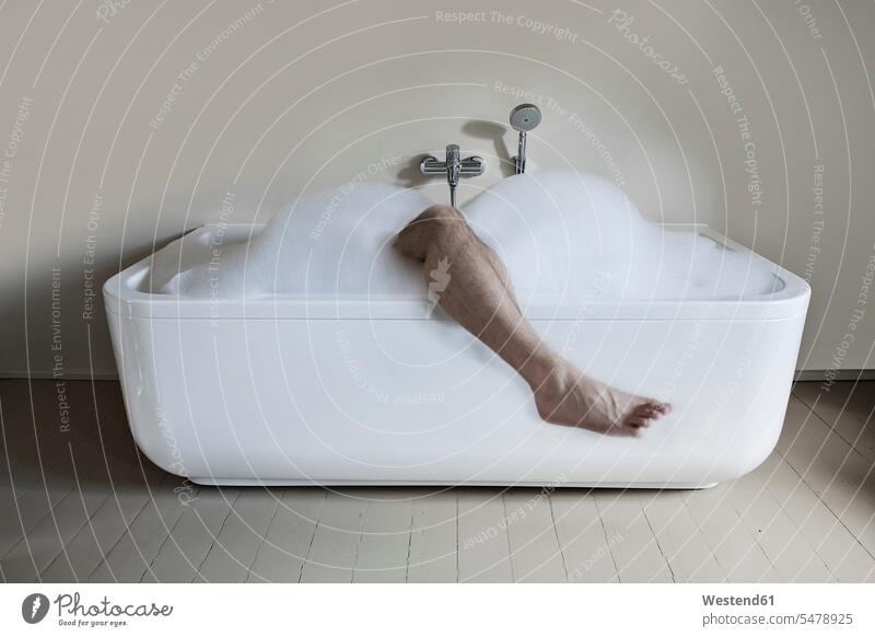 Mid adult man in bathtub with leg out pampering living habitation rooming copy space caucasian european caucasian ethnicity caucasian appearance soapsuds lather