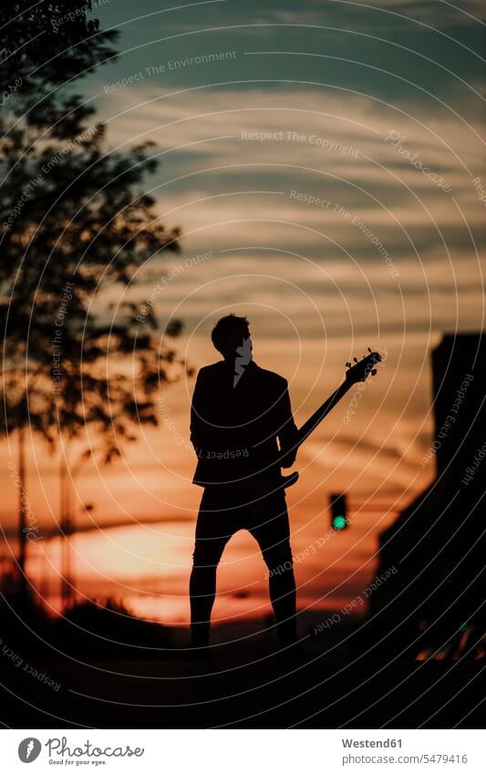 Silhouette of musician playing bass guitar while standing on road color image colour image outdoors location shots outdoor shot outdoor shots sunset sunsets