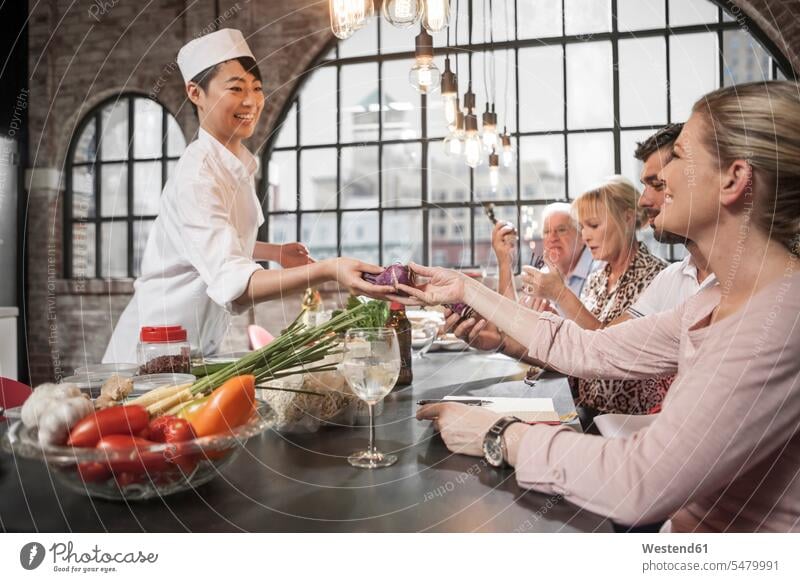 Female chef handing over beetroot to female student in cooking class female cook group of people Group groups of people smiling smile cooks Chefs persons