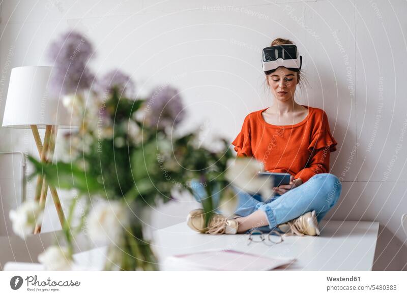 Young woman sitting on table using tablet wearing VR glasses Flower Flowers vase vases digitizer Tablet Computer Tablet PC Tablet Computers iPad Digital Tablet