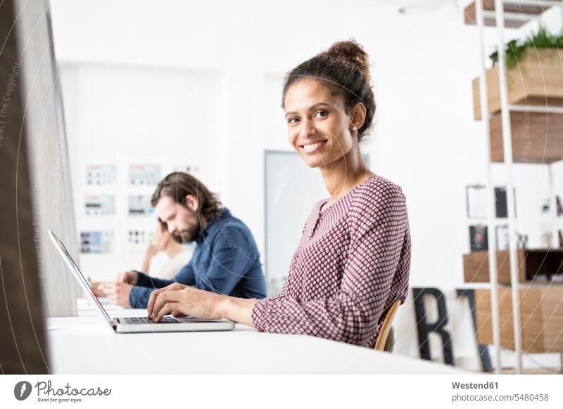 Smiling woman in office working on laptop At Work offices office room office rooms colleagues workplace work place place of work smiling smile Laptop Computers