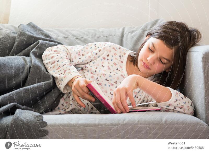 Girl lying on the couch reading a book books girl females girls child children kid kids people persons human being humans human beings settee sofa sofas couches