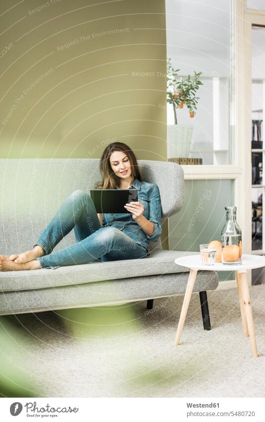 Young woman sitting on the couch using tablet digitizer Tablet Computer Tablet PC Tablet Computers iPad Digital Tablet digital tablets settee sofa sofas couches