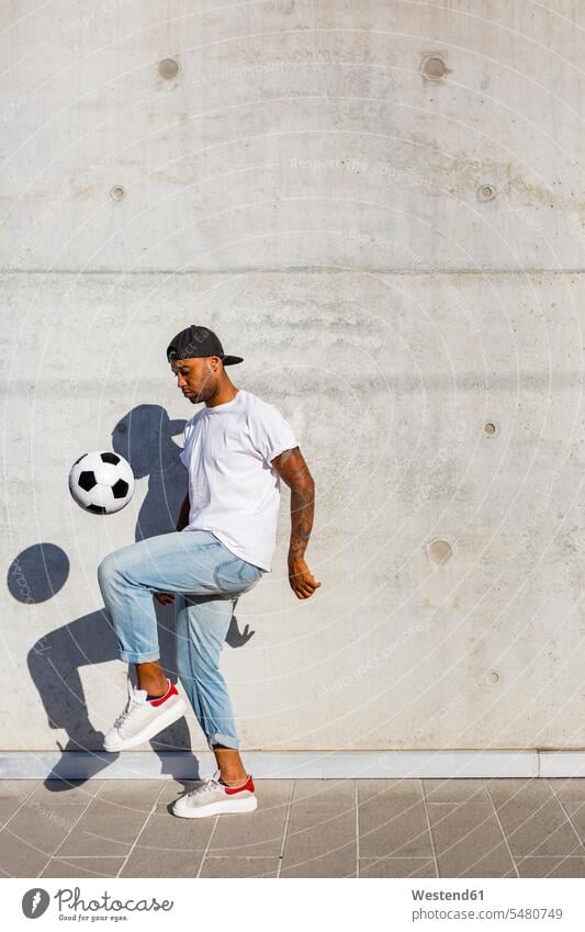 Young man playing with soccer ball in front of concrete wall kicking soccer balls footballs men males Adults grown-ups grownups adult people persons human being