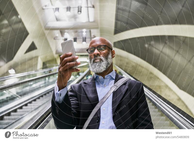 Businessman with smartphone reading messages on escalator on the move on the way on the go on the road text messaging SMS Text Message Smartphone iPhone