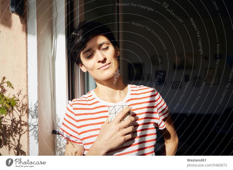 Woman with cup of coffee on balcony enjoying the sunshine sunlight Sunlit balconies Coffee Cup Coffee Cups smiling smile indulgence enjoyment savoring indulging