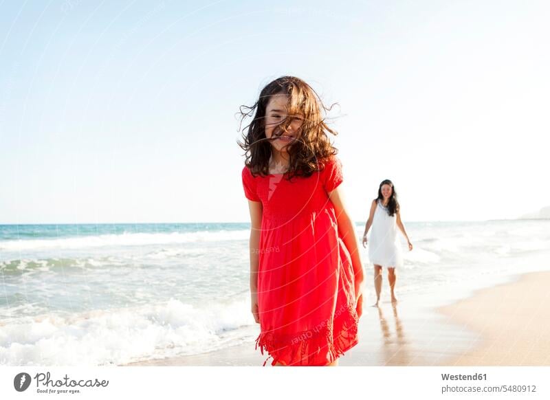 Happy little girl on the beach with her mother in the background smiling smile females girls child children kid kids people persons human being humans