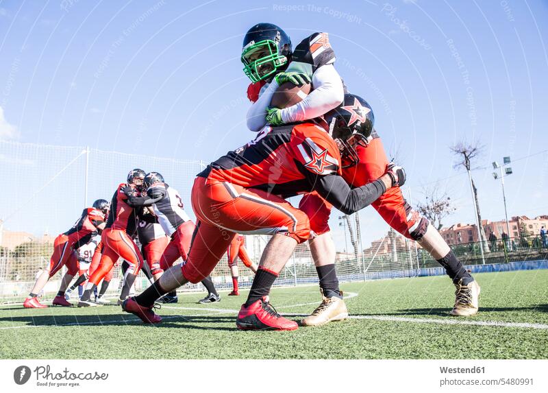 American football player being tackled by opponent player during a match Football helmet helmets Protective Headwear sport sports sports field sports fields