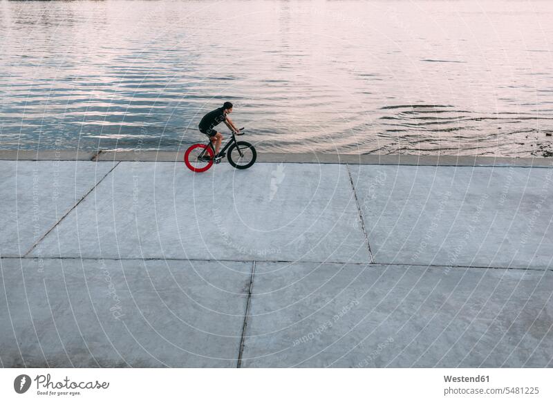 Young man riding fixie bike at the waterfront River Rivers driving drive men males bicycle bikes bicycles waters body of water Adults grown-ups grownups adult