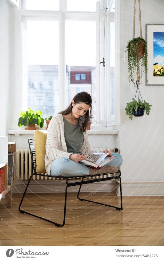 Woman at home sitting on chair reading book Seated woman females women books Adults grown-ups grownups adult people persons human being humans human beings