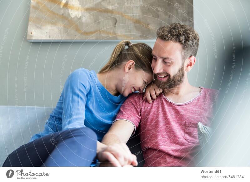 Happy young couple sitting on couch Seated happiness happy laughing Laughter twosomes partnership couples positive Emotion Feeling Feelings Sentiments Emotions