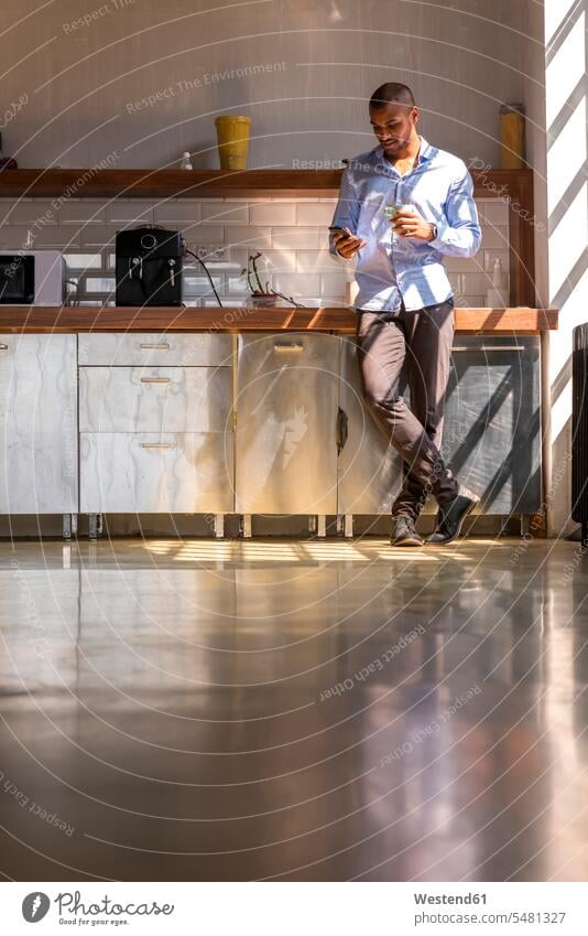 Young entrepreneur standing in company kitchen, drinking coffee, using smartphone Taking a Break resting break reading young entrepreneur young entrepreneurs