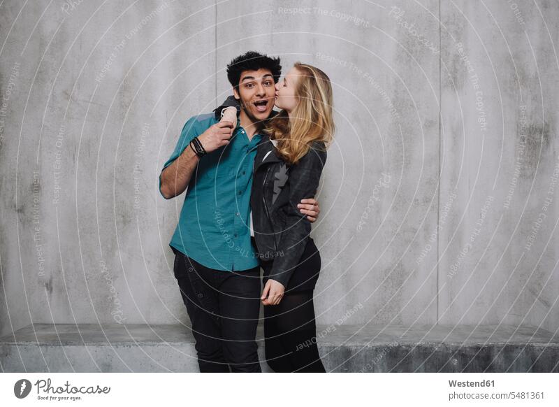 Couple in front of concrete wall, kissing kisses smiling smile peck pecks Joy enjoyment pleasure Pleasant delight happiness happy couple twosomes partnership