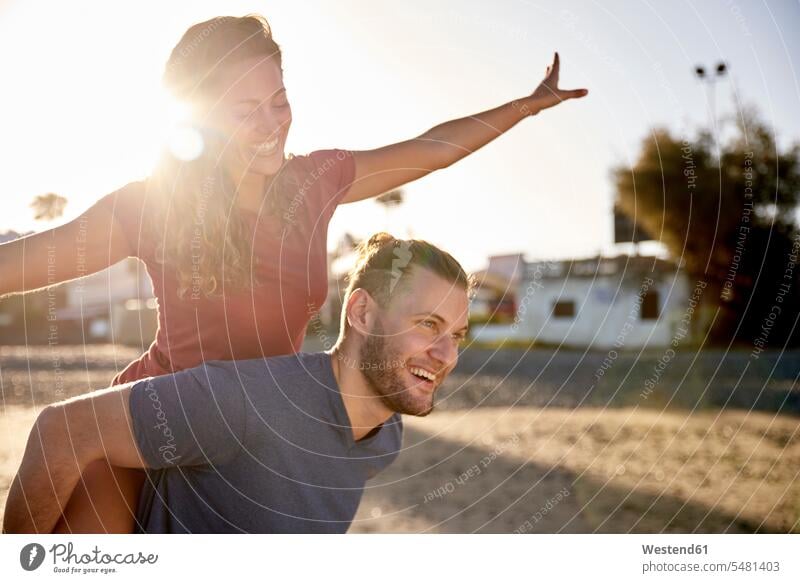 Young man giving his girlfriend a piggyback ride on the beach beaches friends piggy-back pickaback Piggybacking Piggy Back couple twosomes partnership couples