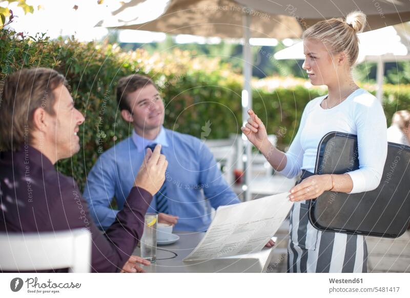 Waitress talking to two businessmen at outside restaurant waitress waitresses garden restaurant waiter server waiters service Wait Staff restaurants ordering