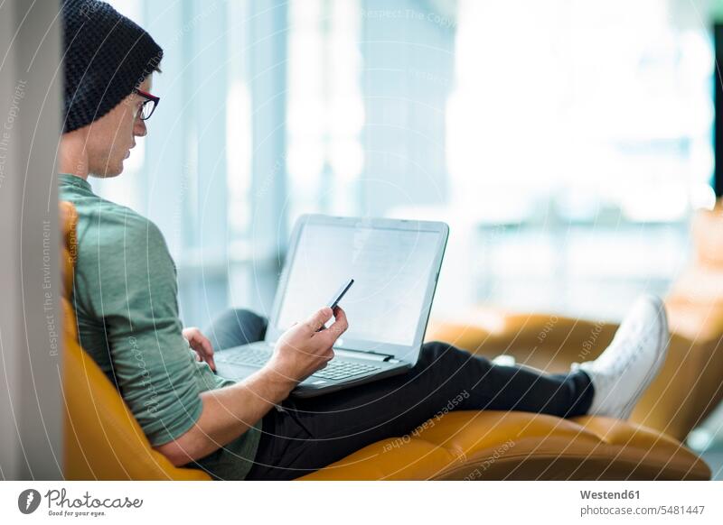 Young man working in armchair, using laptop Arm Chairs armchairs Laptop Computers laptops notebook At Work sitting Seated Concentration concentrating