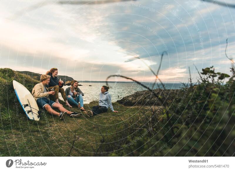 Happy friends with surfboard and drinks socializing at the coast at sunset drinking surfboards happiness happy coastline shoreline surfing surf ride surf riding