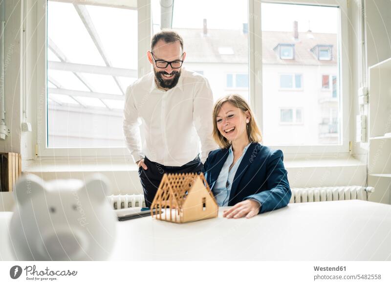 Laughing woman and man with house model and piggy bank in office Piggybank piggy banks businesswoman businesswomen business woman business women models offices