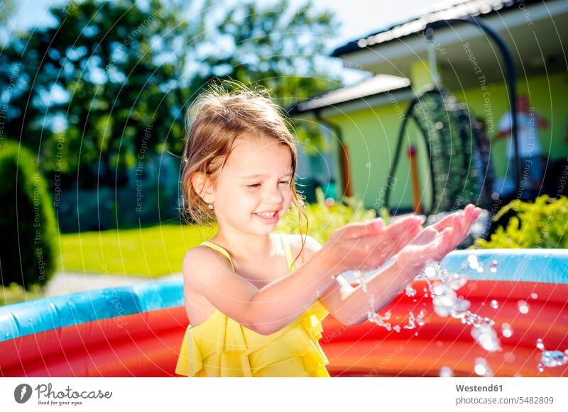 Little girl having fun in paddling pool in the garden females girls splashing child children kid kids people persons human being humans human beings gardens