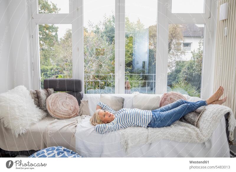 Happy senior woman relaxing on couch in the living room living rooms livingroom senior women elder women elder woman old females settee sofa sofas couches