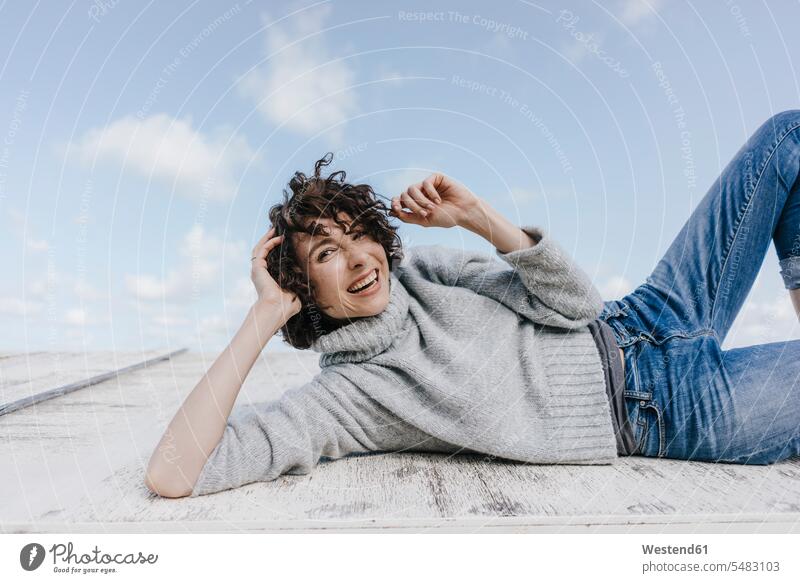 Happy woman lying on wooden box laughing Laughter females women laying down lie lying down relaxed relaxation positive Emotion Feeling Feelings Sentiments